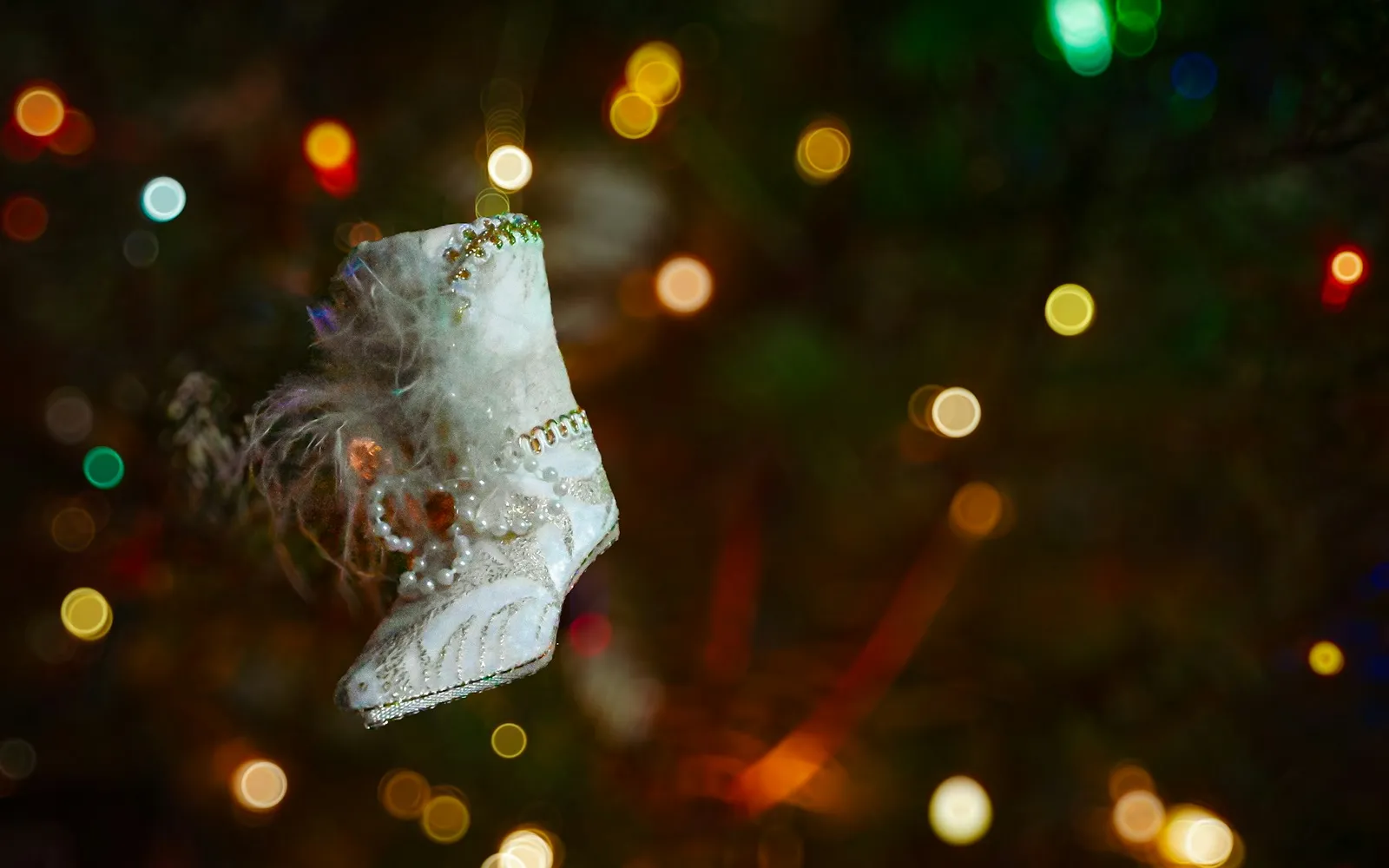 A small white boot ornament hanging on a Christmas tree, with blurred lights behind it