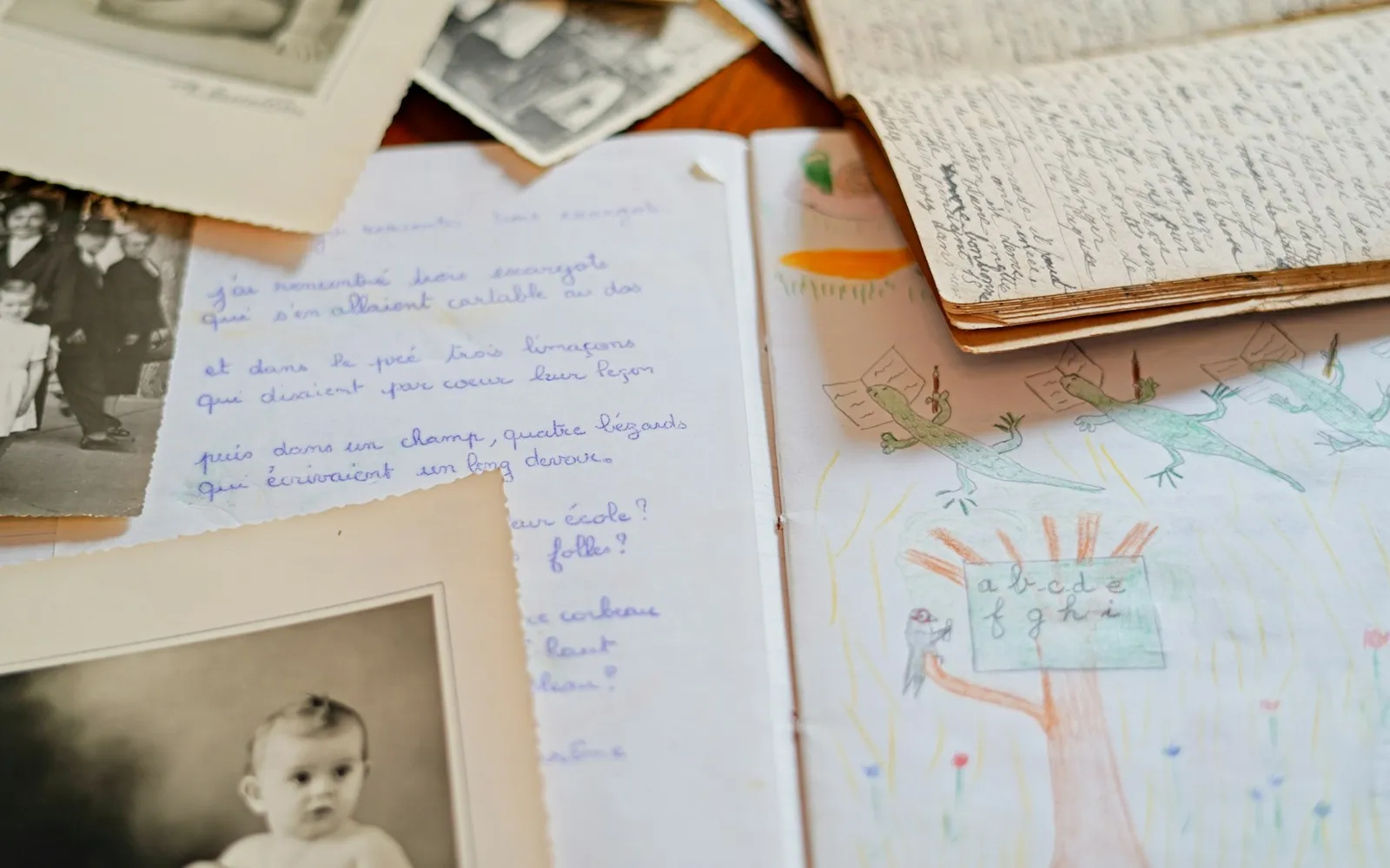 Old family photos, a baby's portrait, handwritten pages and a child's drawing spread across a table